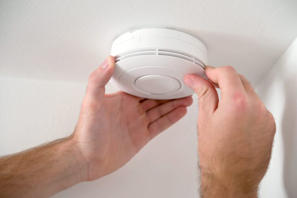Electrician fitting a mains-wired smoke alarm to a ceiling